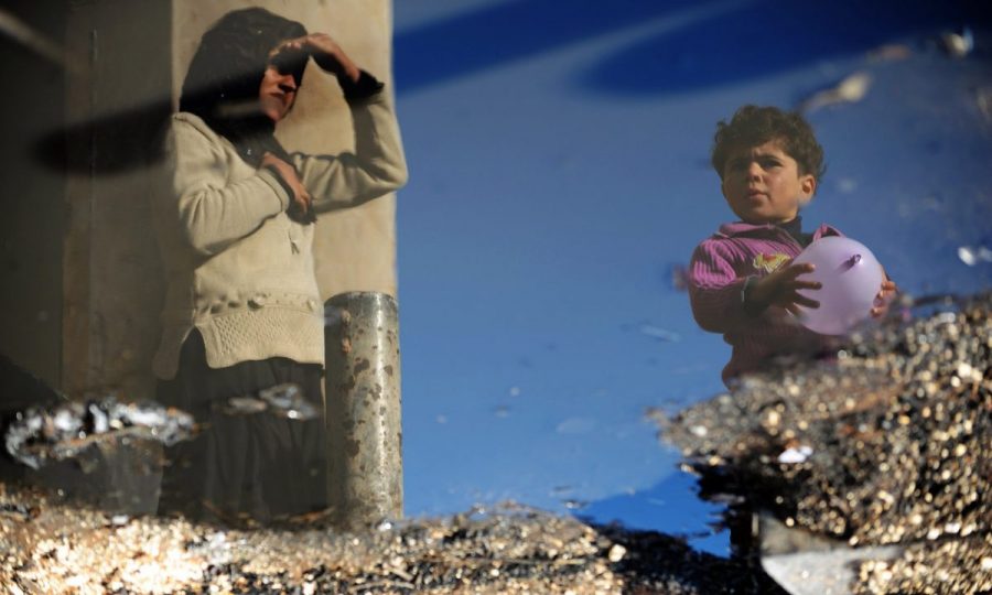 A Syrian internally displaced woman and child are reflected in a puddle of water in the Bab al-Hawa camp along the Turkish border in Idlib. Photograph: Bulent Kilic/AFP/Getty Images