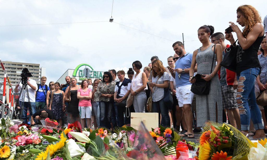 People stand next to flowers laid for the victims of the shooting near the Olympia Einkaufszentrum shopping centre in Munich. Photograph: Christof Stache/AFP/Getty Images