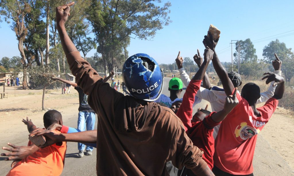 A young man wearing a police helmet joins angry protestors in Harare, 4 July. Photograph: Tsvangirayi Mukwazhi/AP