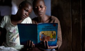 Young women read an educational book at an adolescent youth centre in Uganda. The government has pledged to inject up to $5m a year into family planning. Photograph: Neil Thomas/Getty Images