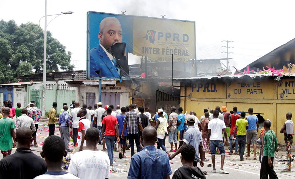 Protesters chant slogans as they destroy the billboard of President Joseph Kabila. Photo: Kenny Katombe/Reuters.