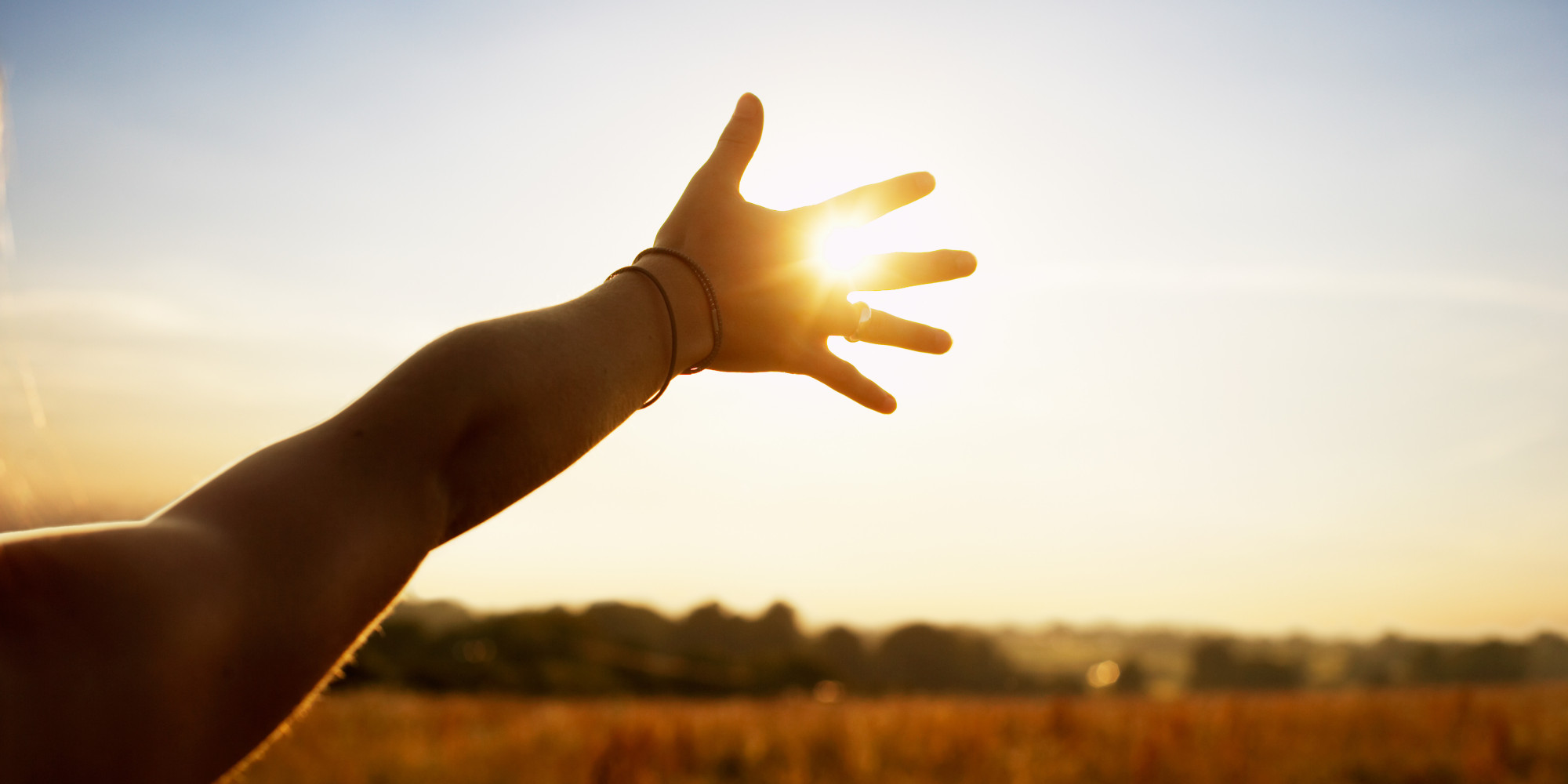Young woman reaching hand towards sun