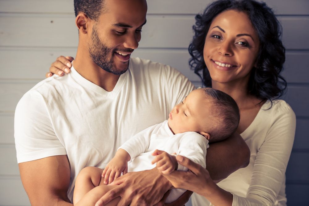Portrait of beautiful young Afro American parents smiling while little baby is sleeping in dad's arms