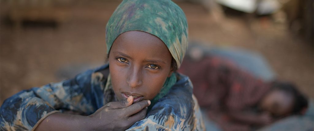 A young girl sits in the shade, while her sister sleeps behind her, at an IDP camp in Baidoa for victims of a drought currently affecting Somalia. UN Photo/Tobin Jones