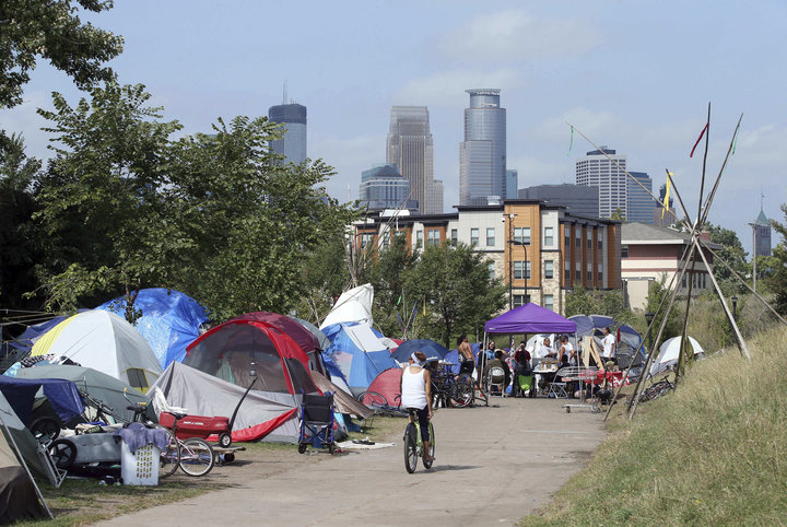 In this Sept. 14, 2018 photo, the Minneapolis skyline rises behind a homeless encampment that continues growing in south Minneapolis. The Minneapolis City Council voted Wednesday, Sept. 26 to approve a temporary site to house hundreds of homeless people who have been living in tents at the encampment just south of downtown. (AP Photo/Jim Mone)