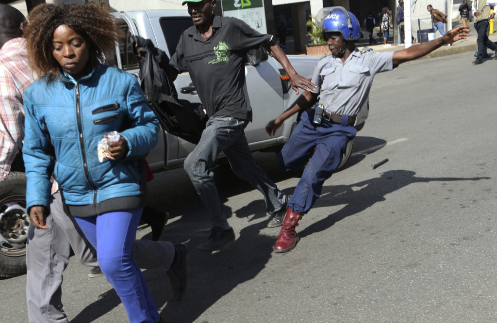 A riot police man kicks out at a man during protests in Harare, Friday, Aug. 16, 2019. The main opposition Movement For Democratic Change party is holding protests over deteriorating economic conditions in the country as well as to try and force Zimbabwean President Emmerson Mnangagwa to set up a transitional authority to address the crisis and organize credible elections. (AP Photo/Tsvangirayi Mukwazhi)
