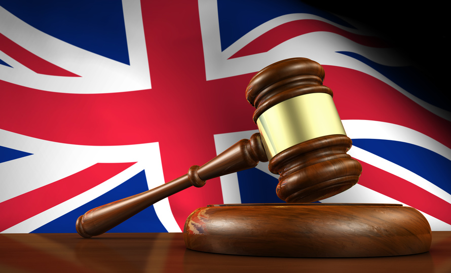 Uk law and justice concept with a 3d render of a gavel on a wooden desktop and the Union Jack flag on background.
