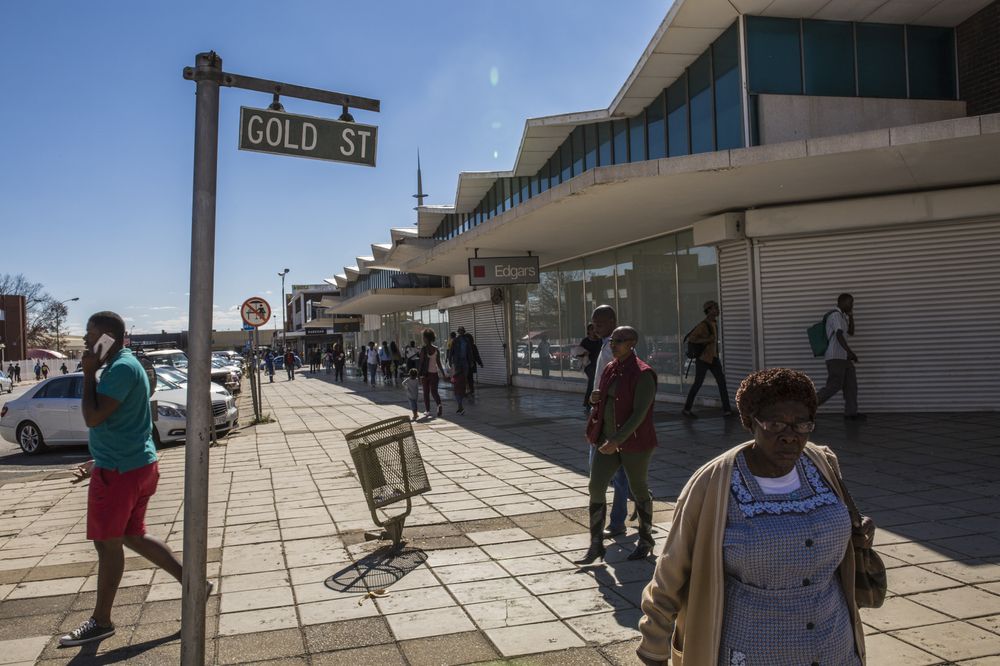 Pedestrians walk by closed-down retail outlets on Gold Street in Carletonville. Photographer: Guillem Sartorio/Bloomberg