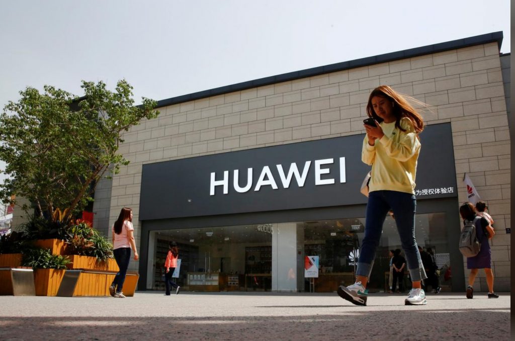 FILE PHOTO: A woman looks at her phone as she walks past a Huawei shop in Beijing, China May 16, 2019. REUTERS/Thomas Peter/File Photo